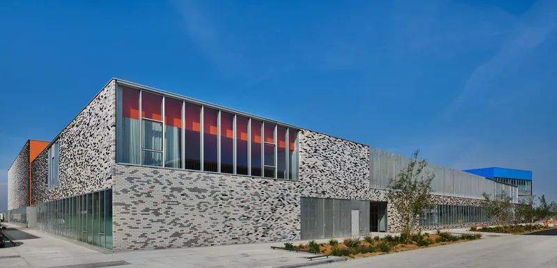 Street view of the variegated brick facade with glazed upper volume and orange panel accents under clear blue sky