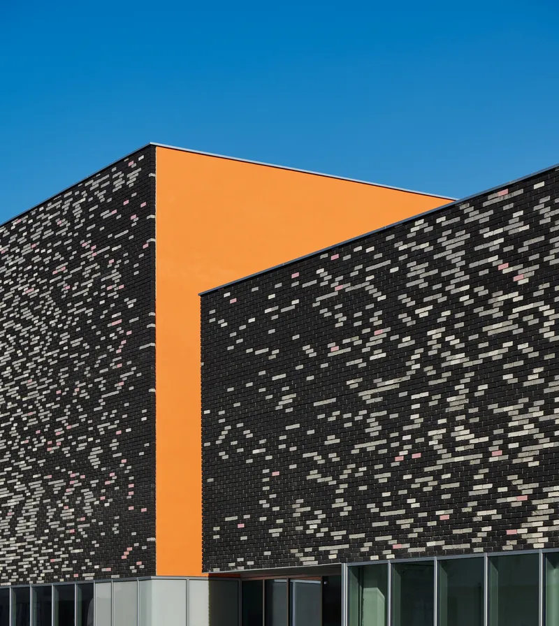 Corner detail of the speckled dark brick wall with orange panel insert framing the glazed base