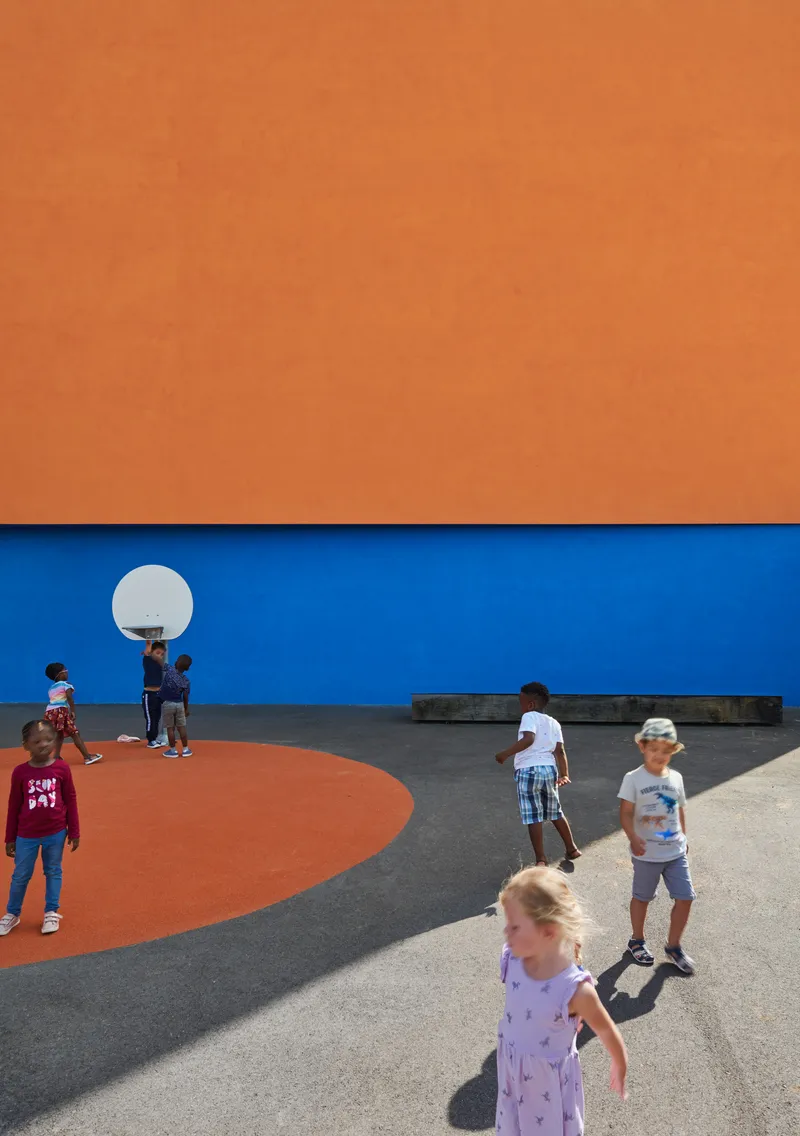 Outdoor basketball court with orange and blue painted walls and children playing under bright sun