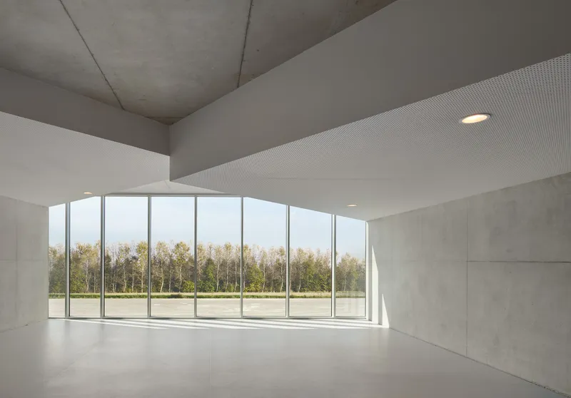 Interior room with concrete walls and ribbed ceiling opening to glazed facade overlooking trees