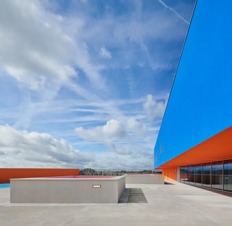 Rooftop terrace with blue and orange facade panels under scattered clouds