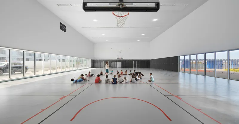 Indoor gymnasium with basketball hoop and court markings while children gather in the center