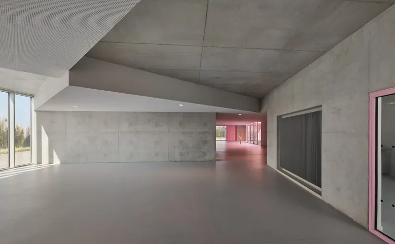 Concrete corridor with exposed ceiling and pink illuminated hallway receding into the distance