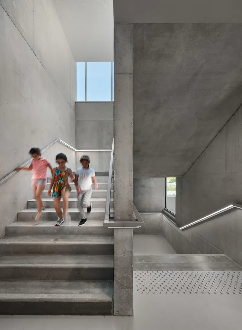 Concrete stairwell with three children descending the steps beneath a skylight window