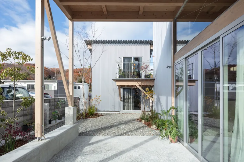 Gravel courtyard with concrete planter bed framed by timber structure and corrugated metal facade in autumn
