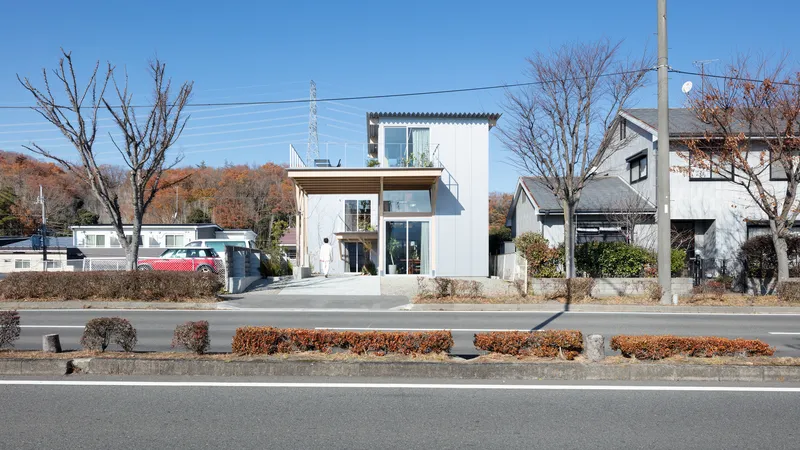 Street view of the white corrugated metal facade with bare trees and median shrubs in autumn