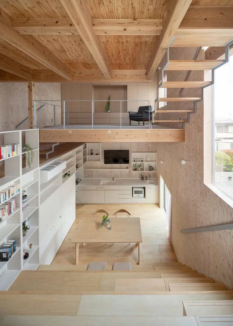 Double-height interior with exposed timber beams, plywood walls, and mezzanine accessed by open treads