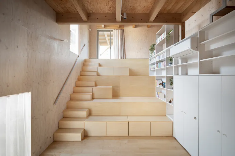 Wide plywood steps with pull-out storage drawers facing white shelving under timber beam ceiling