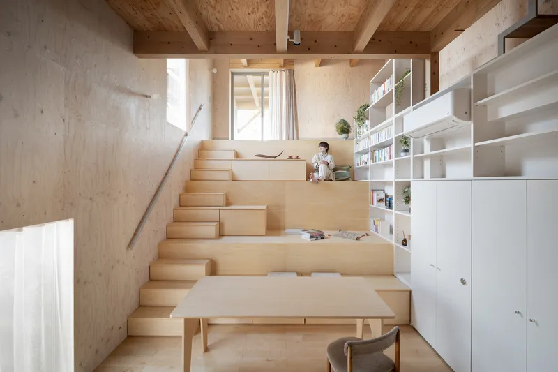 Stepped plywood seating area with a person reading near white shelving and potted plants