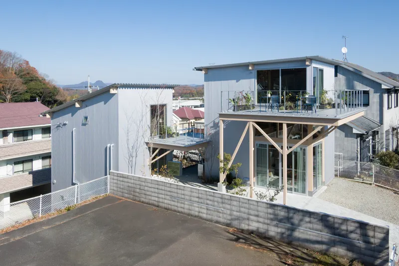 Elevated view of corrugated metal volumes with timber framing and rooftop terrace under a clear blue sky