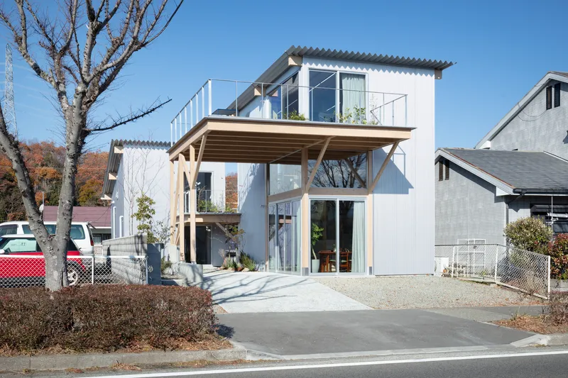 Street facade with exposed timber structure supporting an upper terrace and corrugated metal cladding in winter light