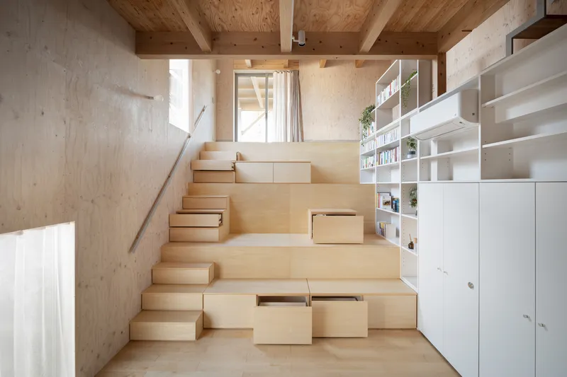 Wide plywood stair with integrated storage drawers and open shelving under exposed timber ceiling beams