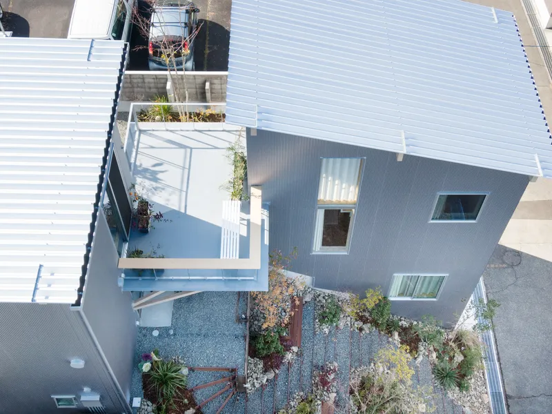 Aerial view of corrugated rooftop with planted gravel courtyard and scattered vegetation between metal-clad volumes
