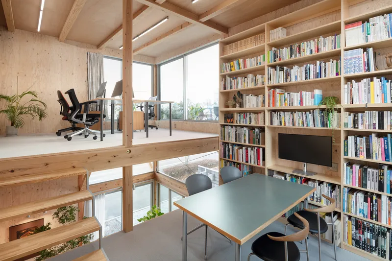 Mezzanine workspace with built-in bookshelf wall and views through the timber frame to lower level