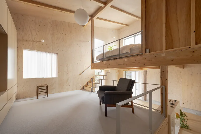Double-height bedroom with vaulted plywood ceiling, suspended globe pendant, and upholstered lounge chair