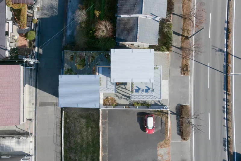 Aerial view showing corrugated metal roofs and a small roof terrace with chairs beside a parked car