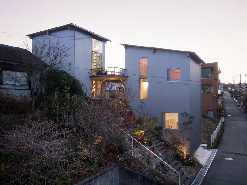 Hillside facade with corrugated metal cladding and illuminated windows at dusk overlooking a sloped landscape