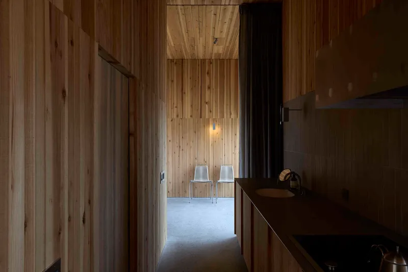 Timber-lined corridor with pendant light leading to two white chairs in adjacent room