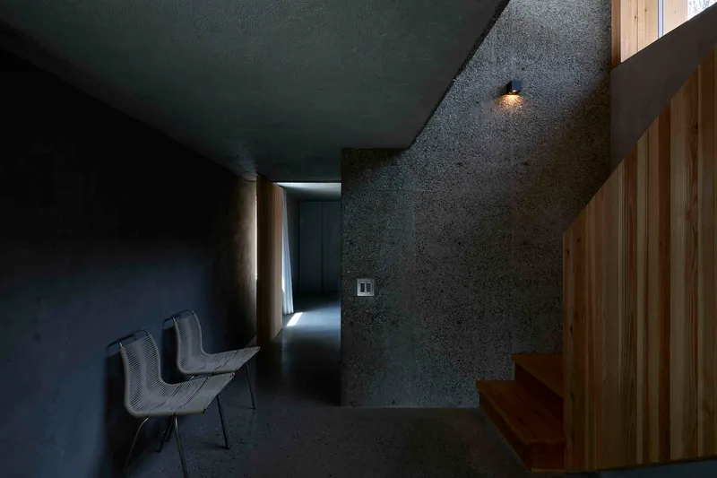 Dark textured concrete corridor with timber partition and recessed wall sconce