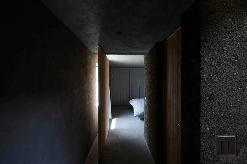 Narrow passage with textured concrete walls and timber door framing bedroom with clerestory light