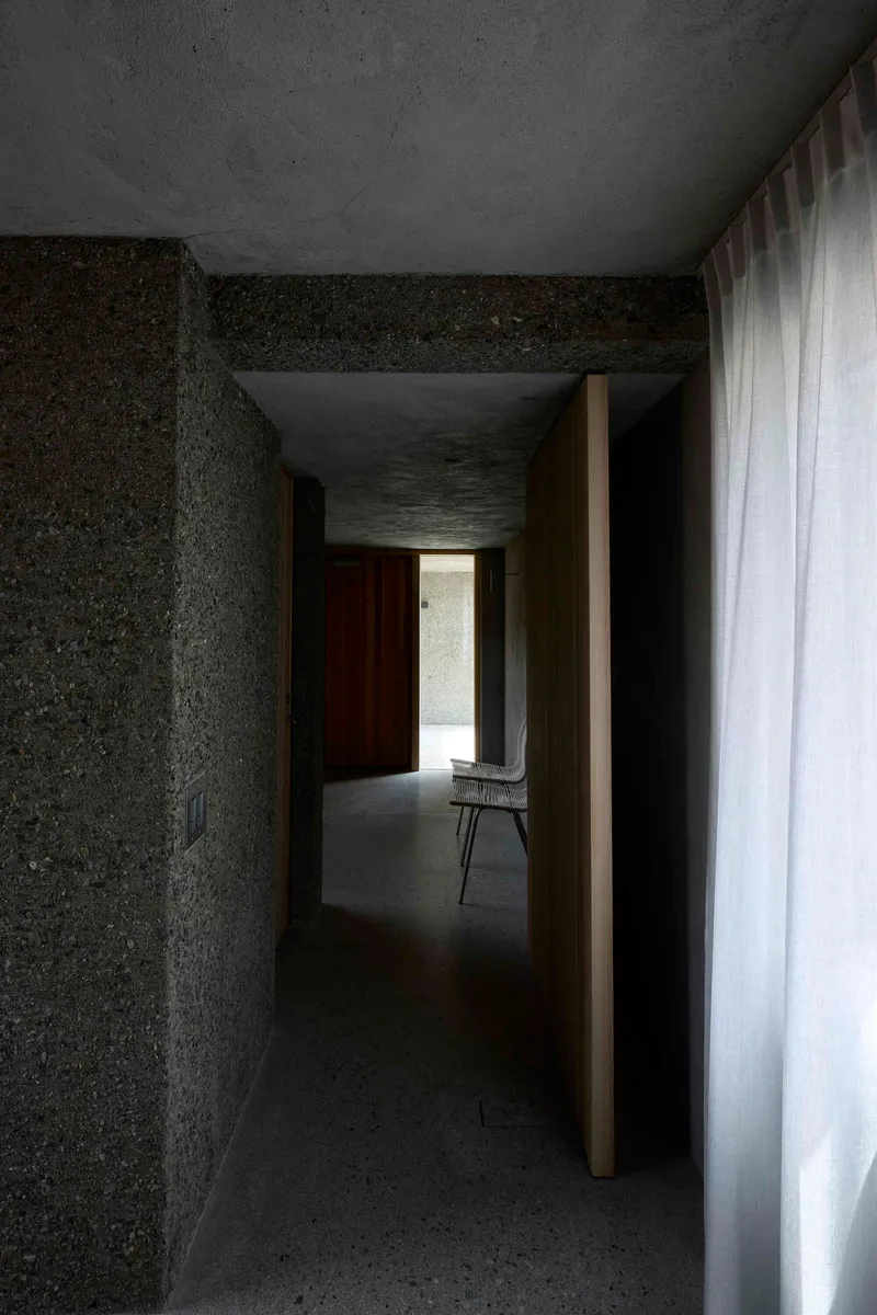Concrete hallway with timber door jamb and chair silhouetted in daylit opening