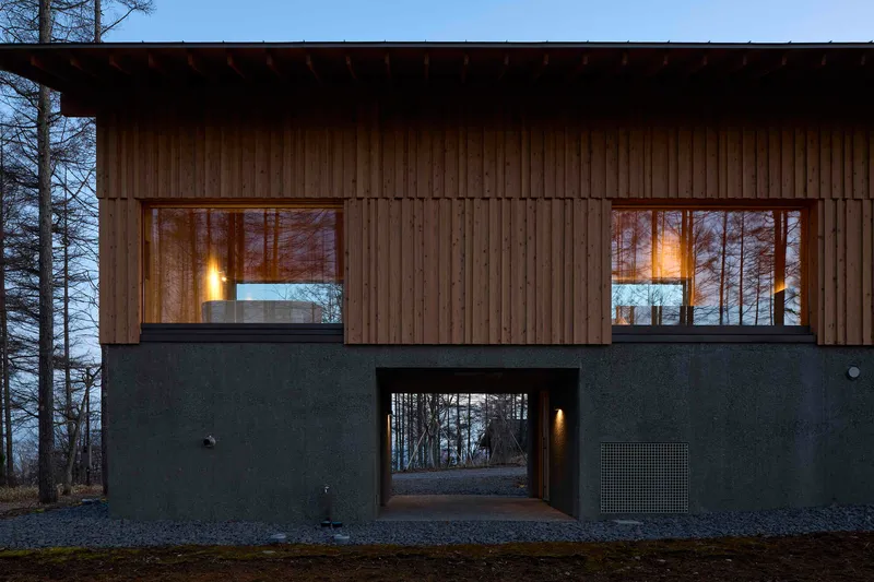 Two-story facade with vertical timber cladding over dark plaster base and covered passageway at dusk