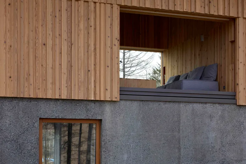 Facade detail showing vertical timber cladding above a concrete base with recessed window
