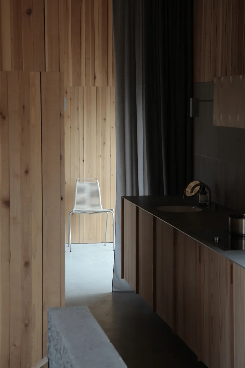 Narrow bathroom corridor with timber cladding and metal chair beside the vanity