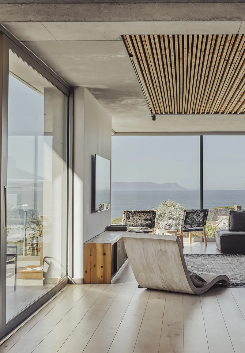 Living room with timber slatted ceiling panel, concrete soffit and floor-to-ceiling glazing facing the sea