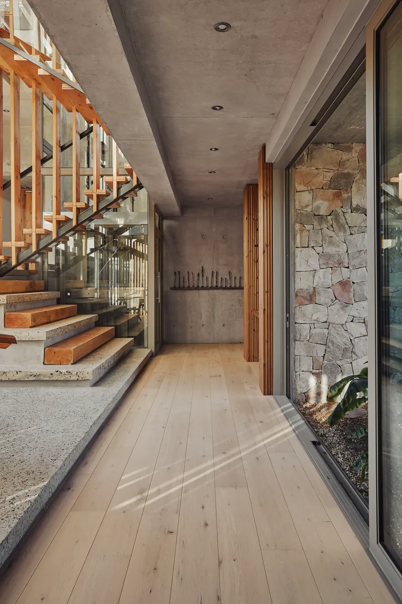 Interior corridor with pale timber flooring alongside open timber staircase and stone accent wall