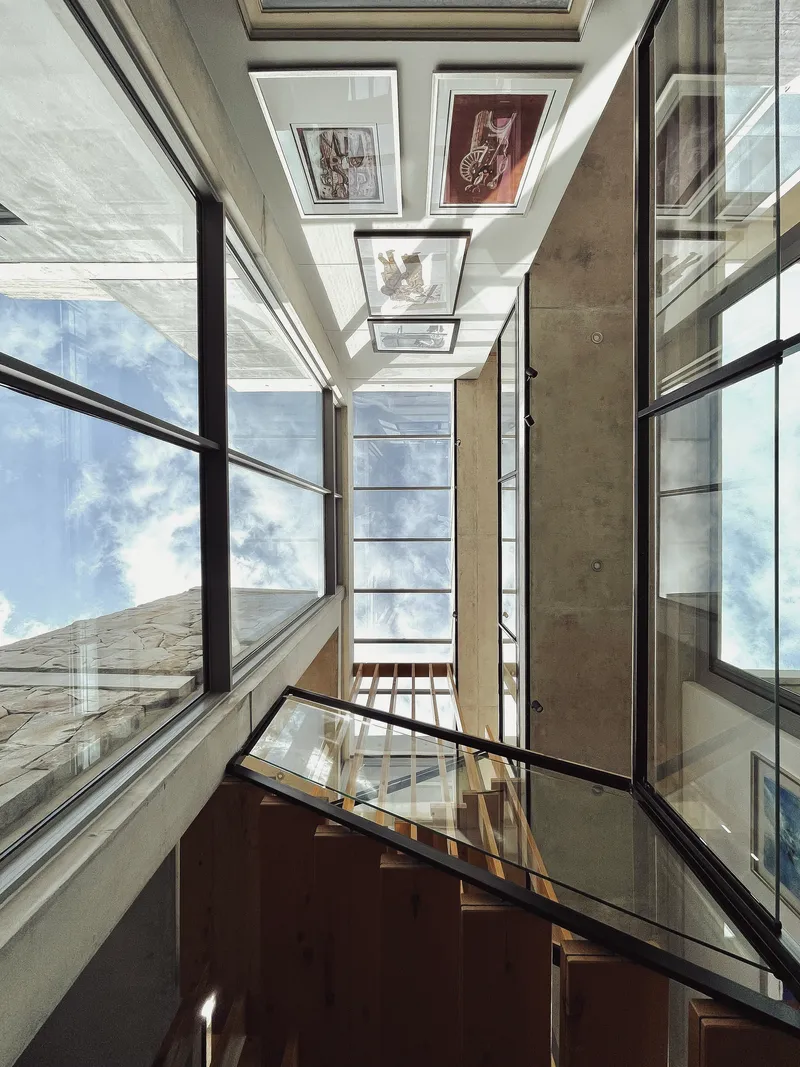 Upward view of a multi-story stairwell with skylights, timber treads and glass balustrades under blue sky