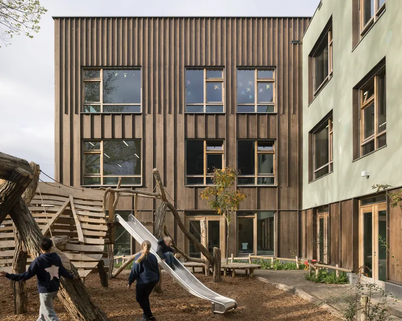 Grid of windows punctuating the vertical timber facade with children playing on a slide below