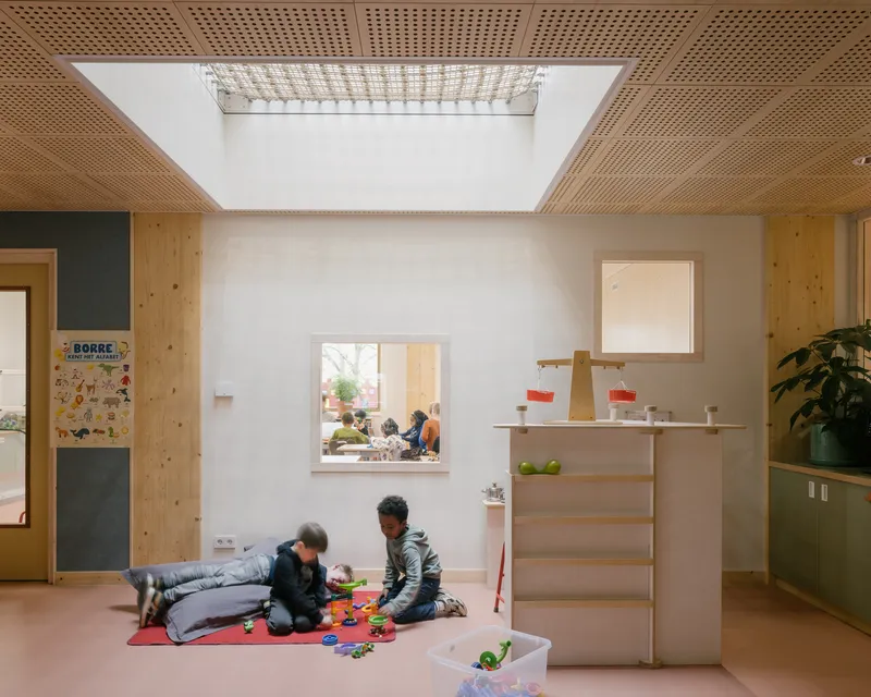 Interior room with perforated timber ceiling skylight and children playing on pink flooring below plywood shelving