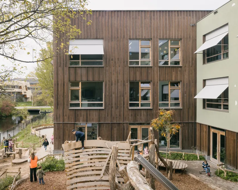 Three-story timber facade with irregularly placed windows overlooking a wooden terrace and play area with children