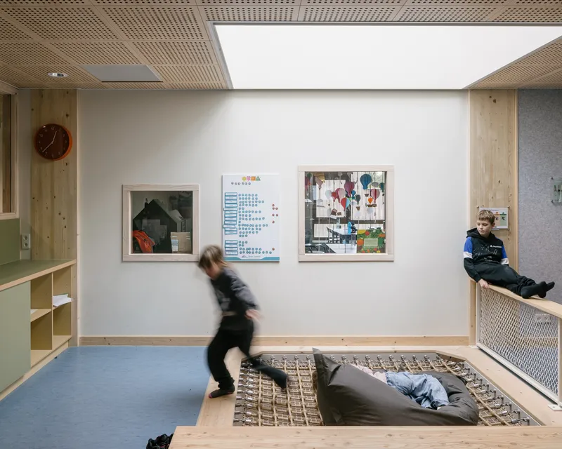 Circulation space with sunken reading pit and children in motion beneath a large skylight