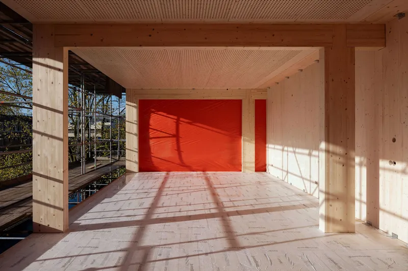Plywood floored room with perforated timber ceiling and red wall panels casting geometric shadows