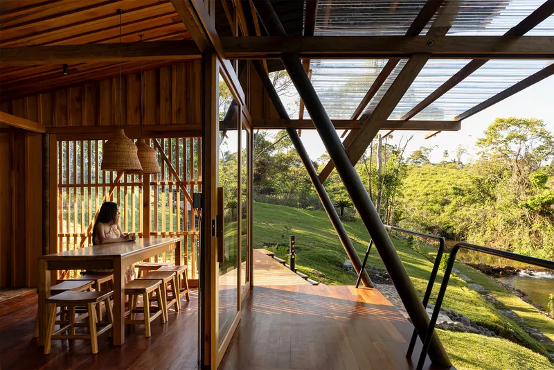 Timber dining space with vertical slat screens and glazed facade opening to sloped lawn