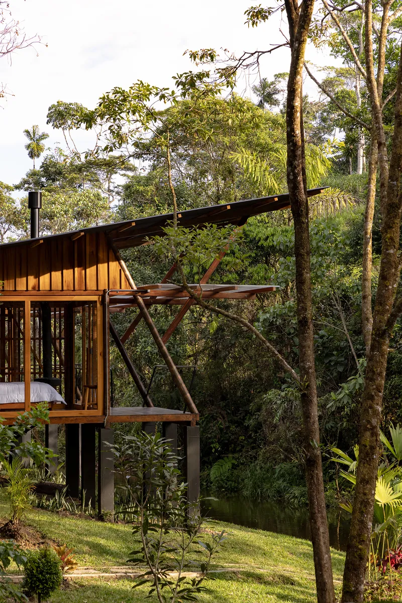 Corner view showing diagonal timber supports and cantilevered roof section above sloped lawn and trees
