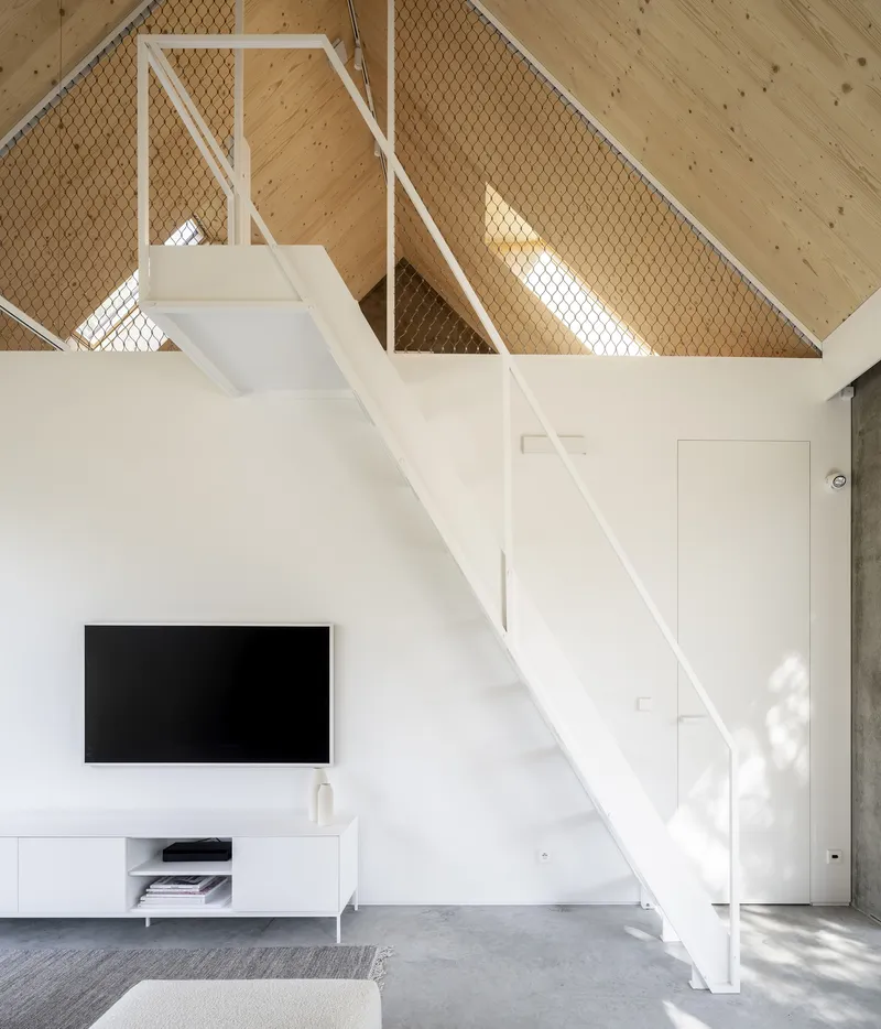 White steel staircase ascending to mezzanine level with wire mesh balustrade panels and timber ceiling