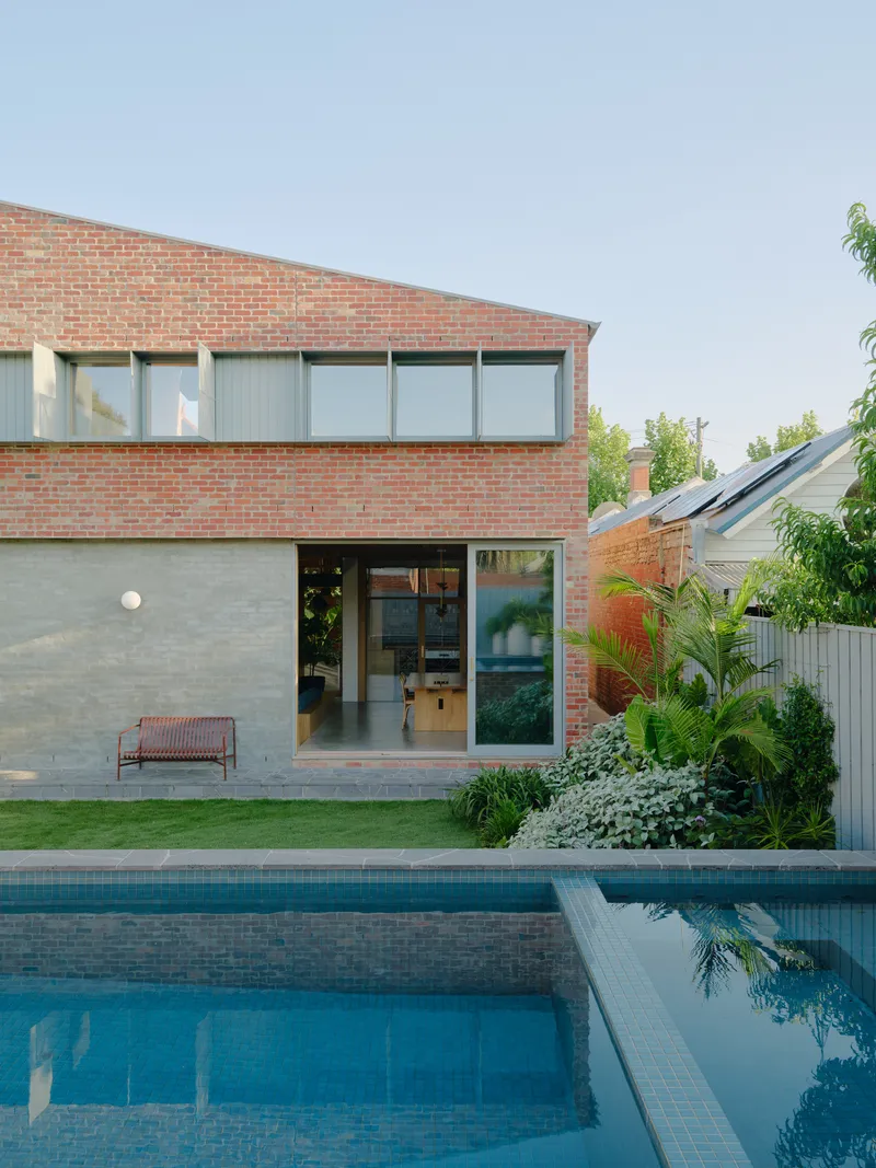 Two-storey brick addition with ribbon windows overlooking a swimming pool and lawn at dusk