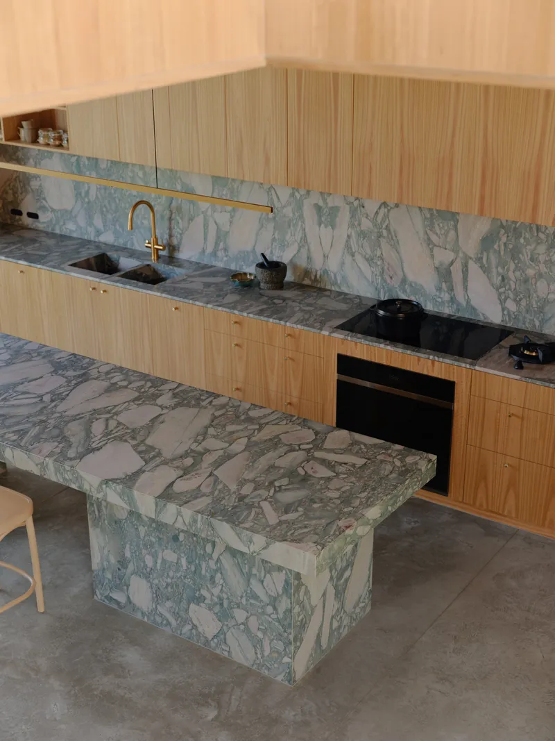Kitchen with pale green veined marble island and backsplash paired with timber veneer cabinetry