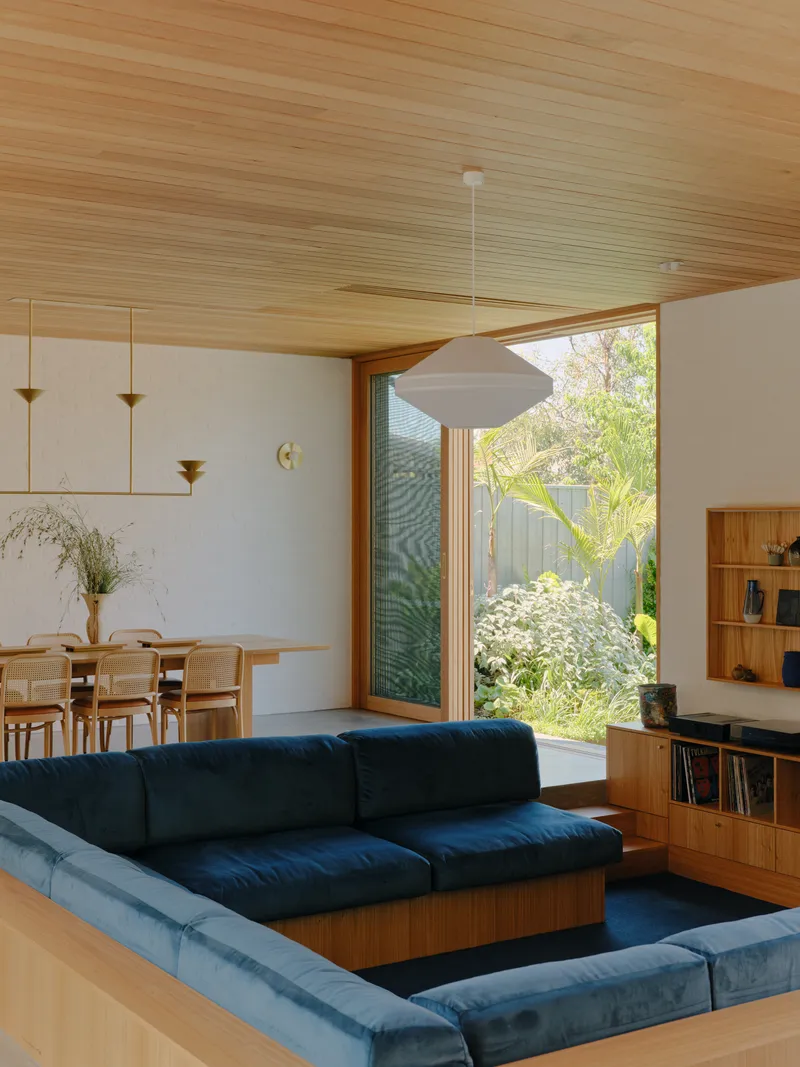 Living room with timber-lined ceiling and glazed doors opening to a planted courtyard
