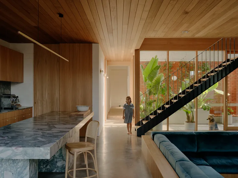 Open-plan interior with black steel staircase ascending past full-height glazing and a person walking