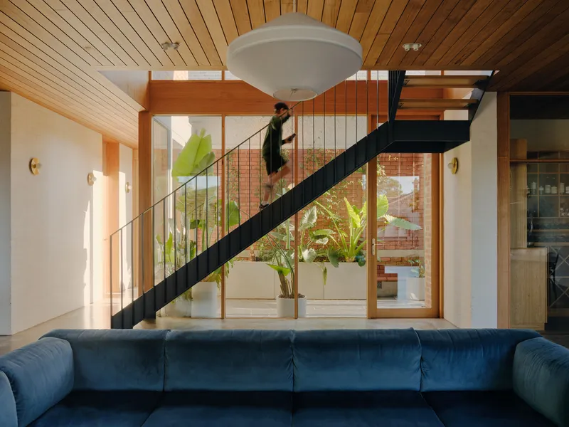 Black steel staircase with slender vertical balusters framing views to an outdoor courtyard with tropical plants