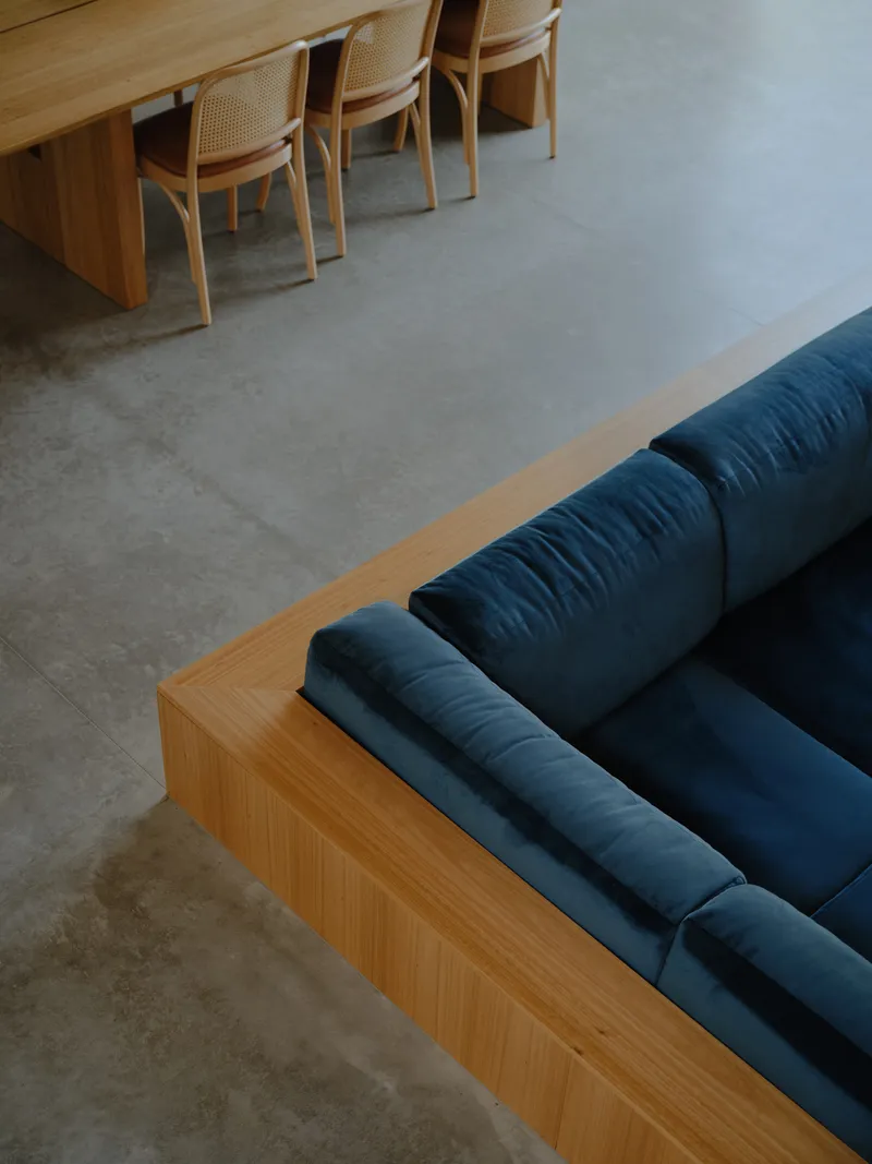 Blue upholstered sofa with timber base on polished concrete floor beside dining table