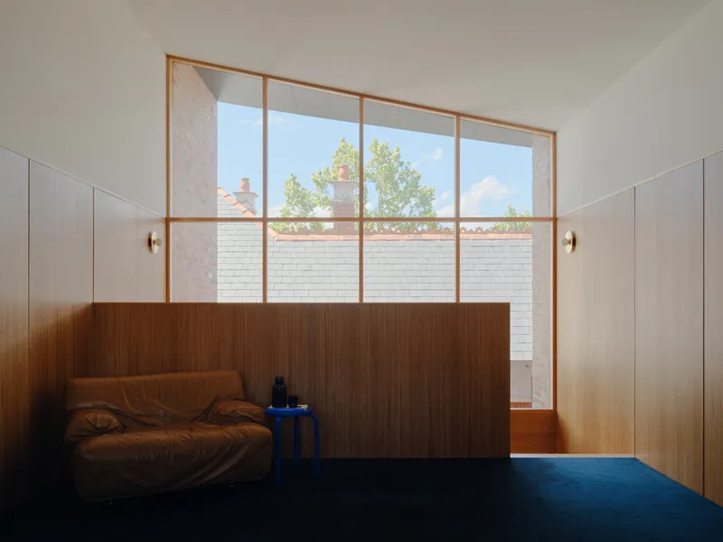 Floor-to-ceiling timber-framed window overlooking courtyard with white brick wall and tree
