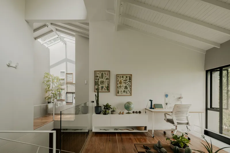 Upper level workspace with exposed white timber rafters and glass balustrade overlooking double-height void