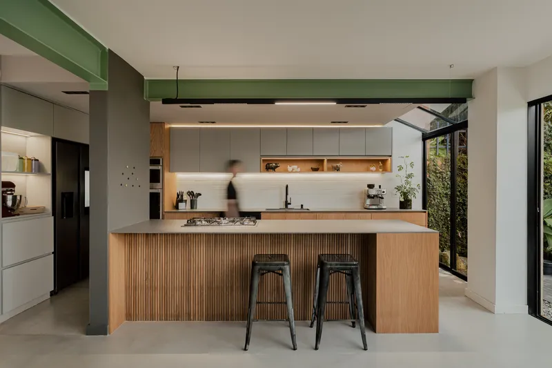 Kitchen island with vertical timber slat cladding beneath green painted beam and pendant lighting