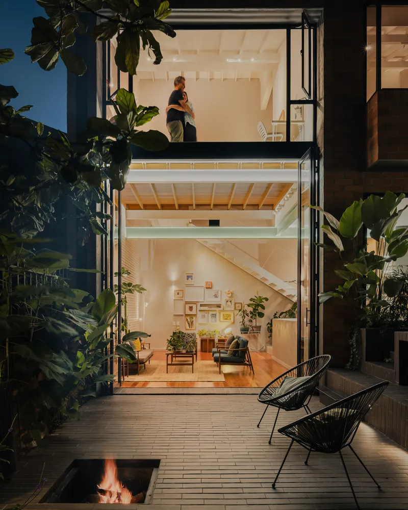 Evening facade showing stacked volumes with timber ceilings framed by lush plantings and timber deck