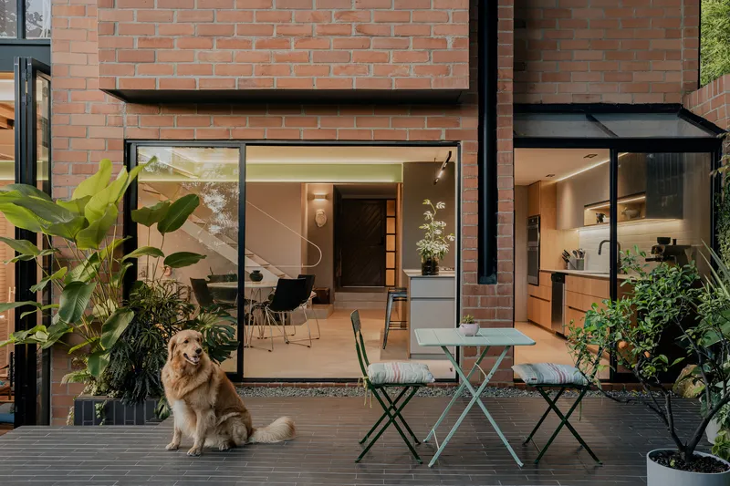 Timber deck with outdoor furniture and a dog facing glazed doors into a brick residence